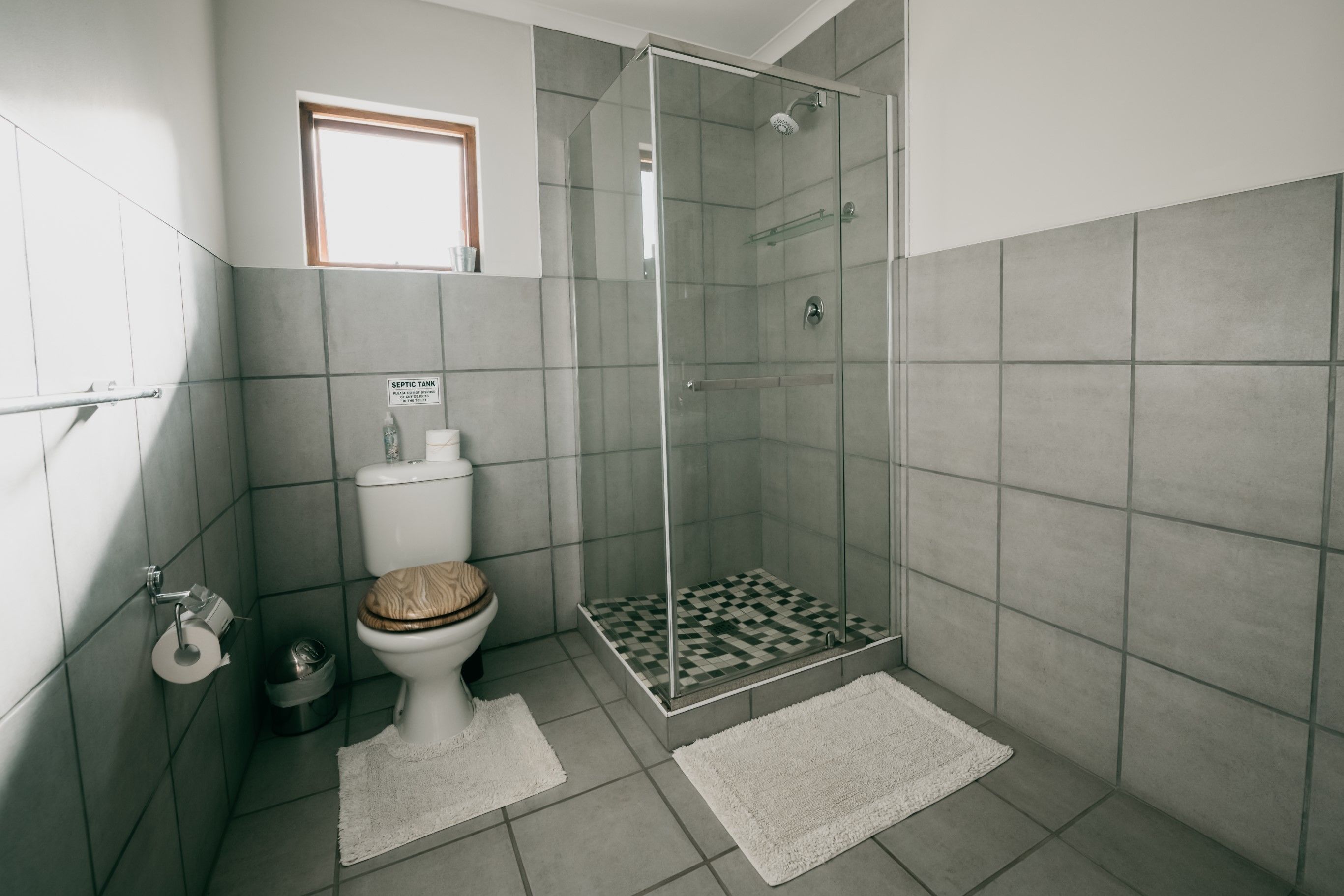 Une salle de bain moderne équipée de toilettes, d’une douche à parois de verre et d’un panneau indiquant la présence d’une fosse septique.
