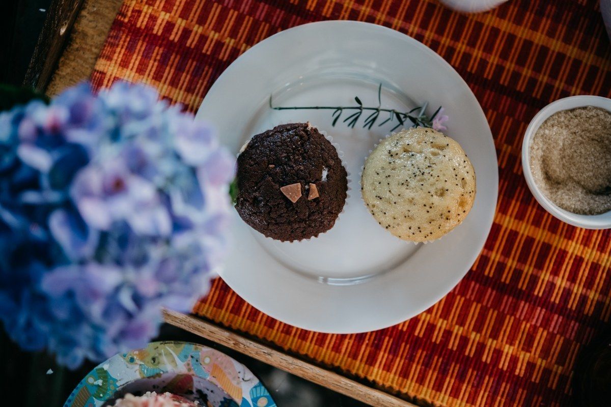 A plate with two cookies, a sprig of rosemary, and a small bowl of sugar on a checkered tablecloth.