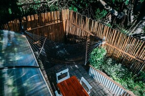 A wooden deck with a metal railing, surrounded by greenery and a bamboo fence.