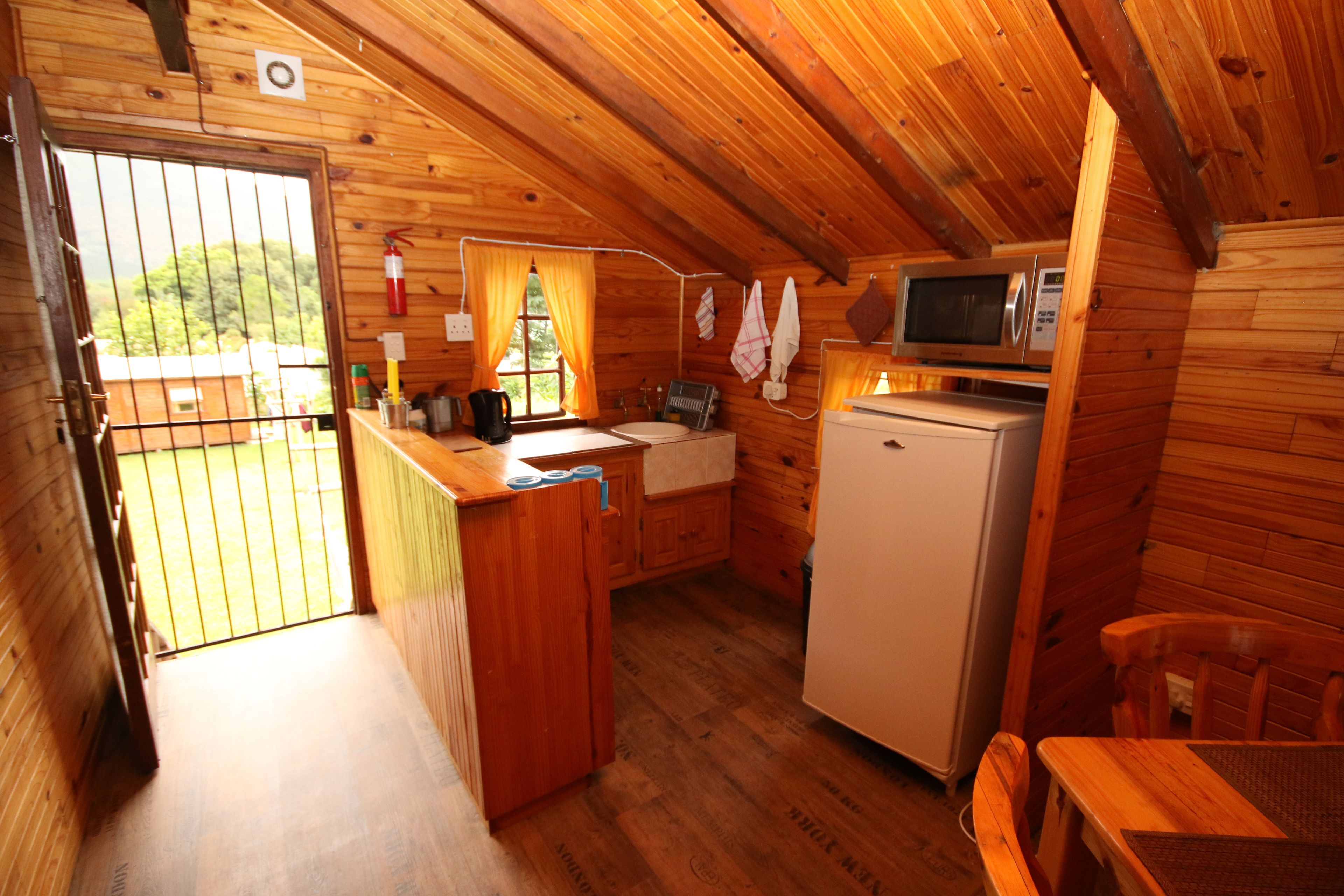 A wooden cabin with a kitchen area including a refrigerator, microwave, and sink.