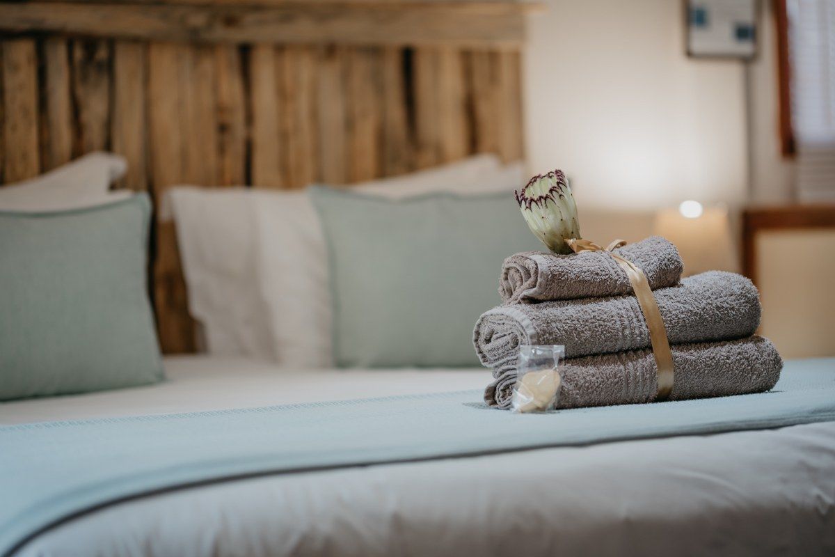 A neatly made bed with rolled towels and a decorative item on top, set against a wooden headboard and light-colored bedding.