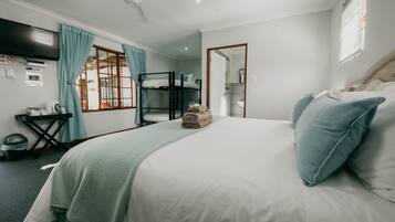 A hotel room with a bunk bed, a desk with a chair, a television, and a window with curtains.