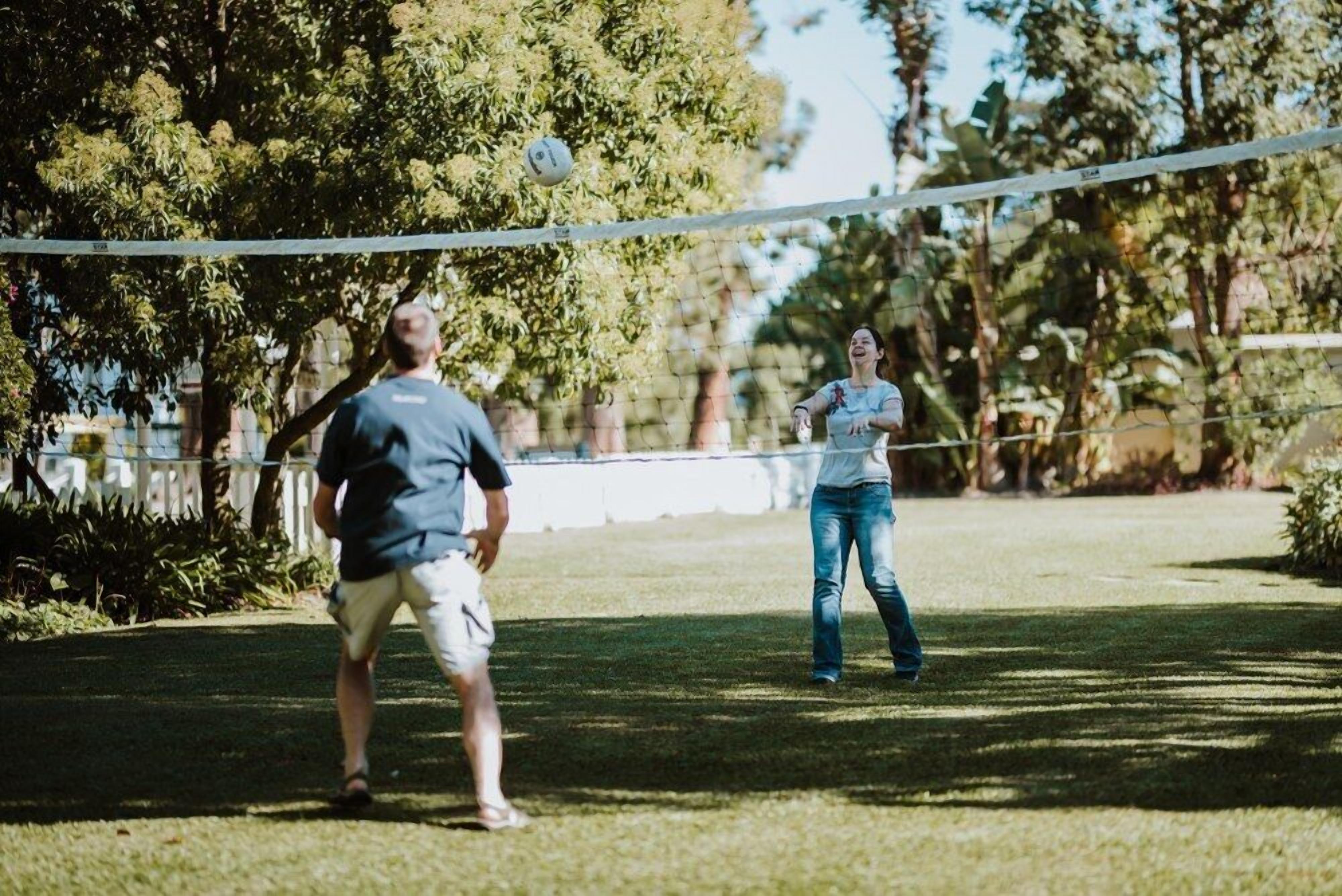 Partido de voleibol al aire libre, con una red y árboles de fondo.