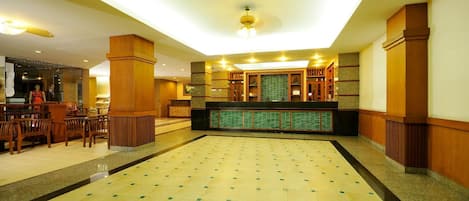 A spacious lobby with a high ceiling, a reception desk, and a seating area with wooden chairs.