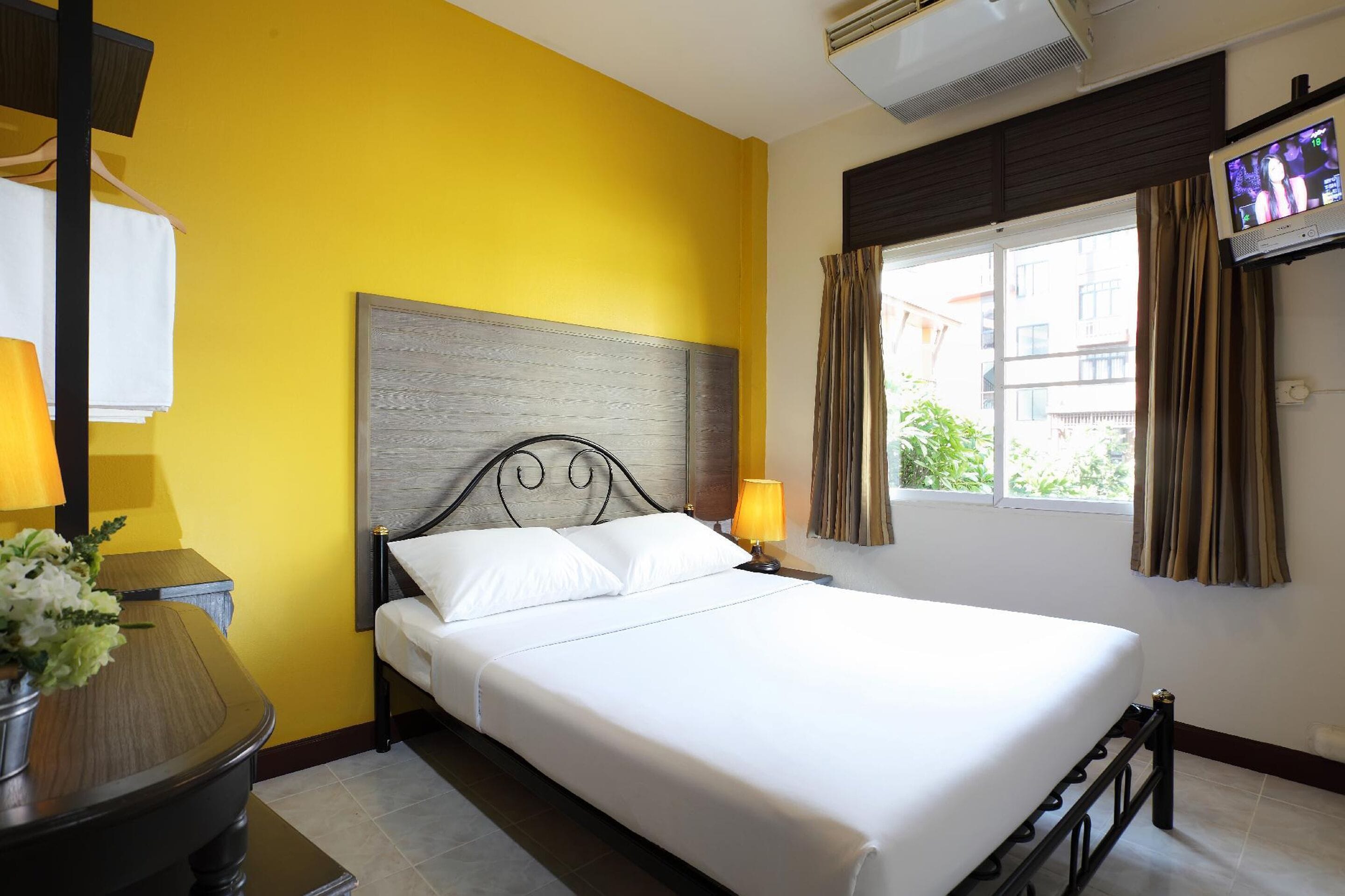 A hotel room with a bed, two bedside lamps, a TV on the wall, and a window with curtains.