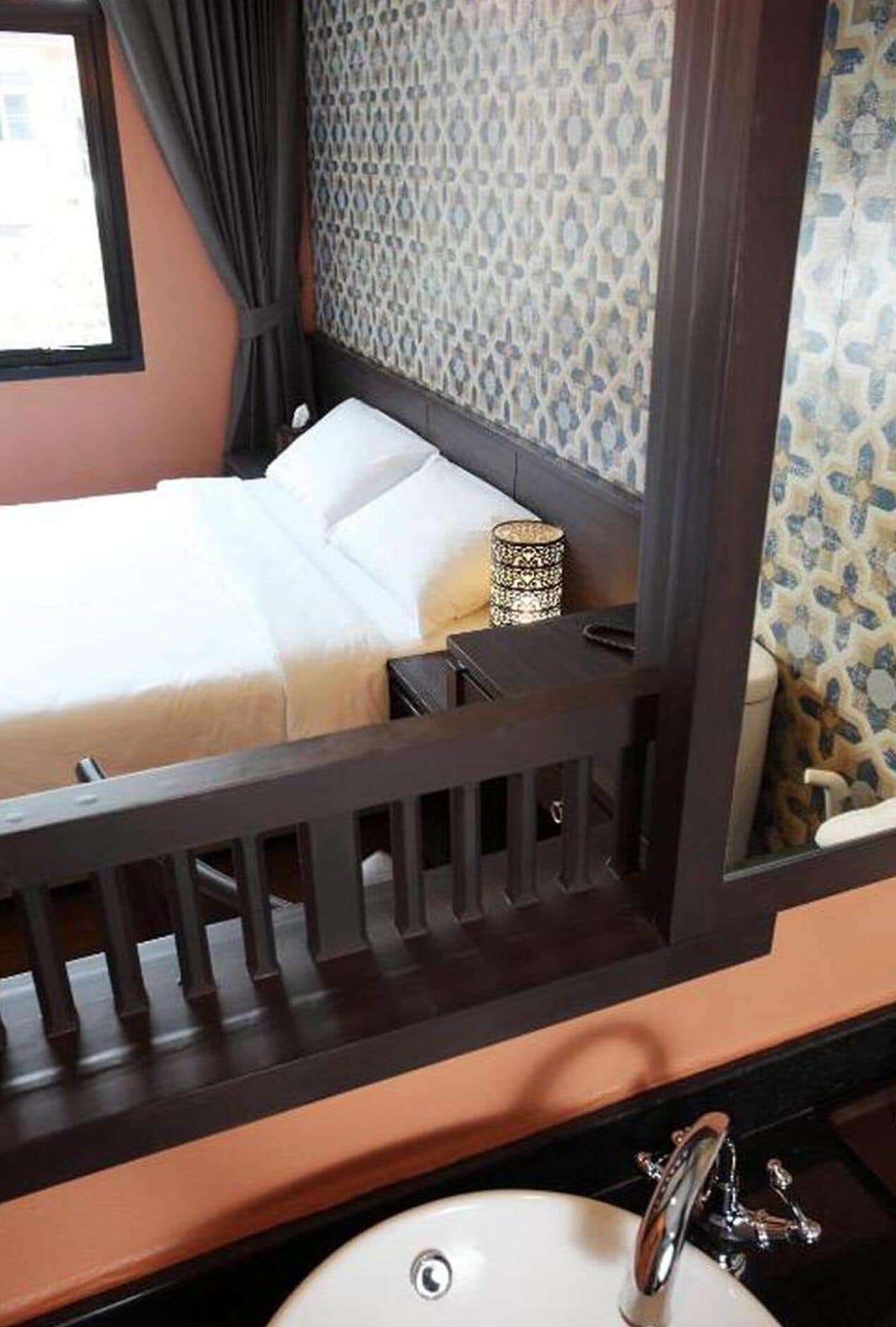 A bedroom with a bed, a nightstand, a lamp, and a bathroom with a sink and mirror.