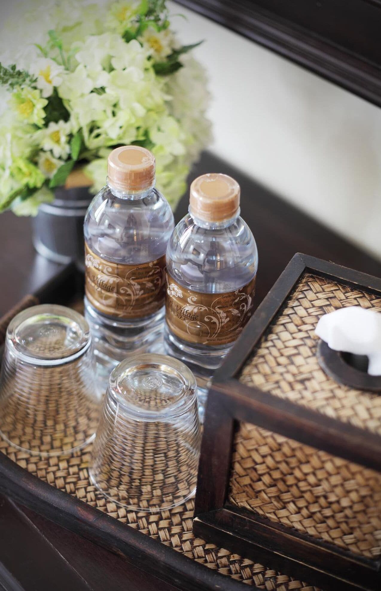 A tray with two bottles and three glasses on a woven mat.