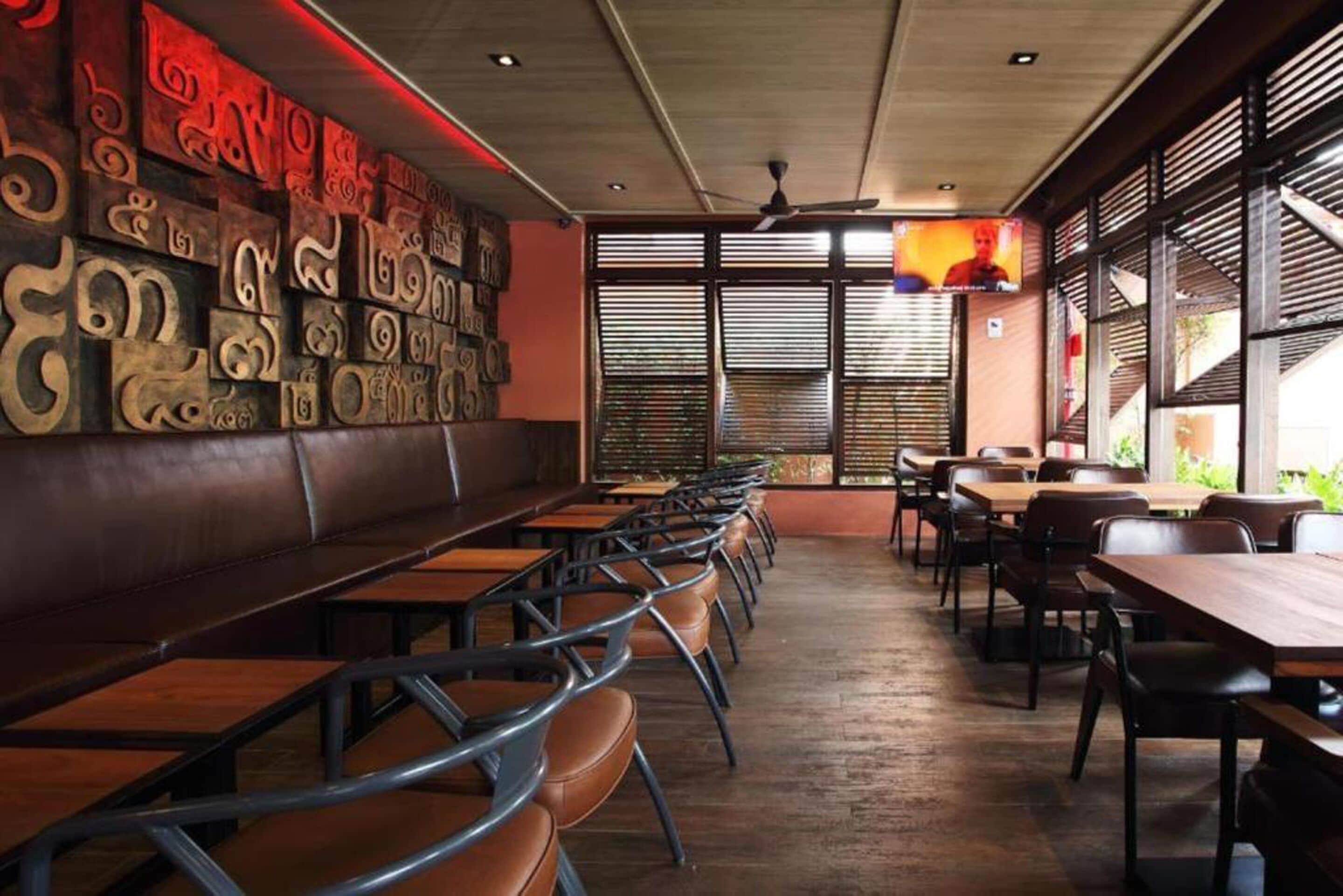 A restaurant with wooden tables and chairs, a high ceiling, and a wall with carved designs.