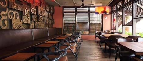 A restaurant with wooden tables and chairs, a high ceiling, and a wall with carved designs.