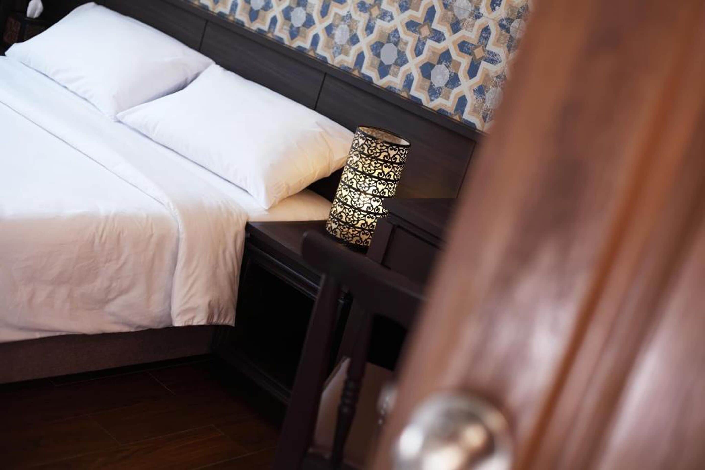 Un letto rifatto con lenzuola bianche, una lampada decorata sul comodino e una parete decorata sullo sfondo.