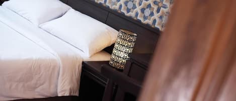 A neatly made bed with white linens, a patterned lamp on the nightstand, and a patterned wall in the background.