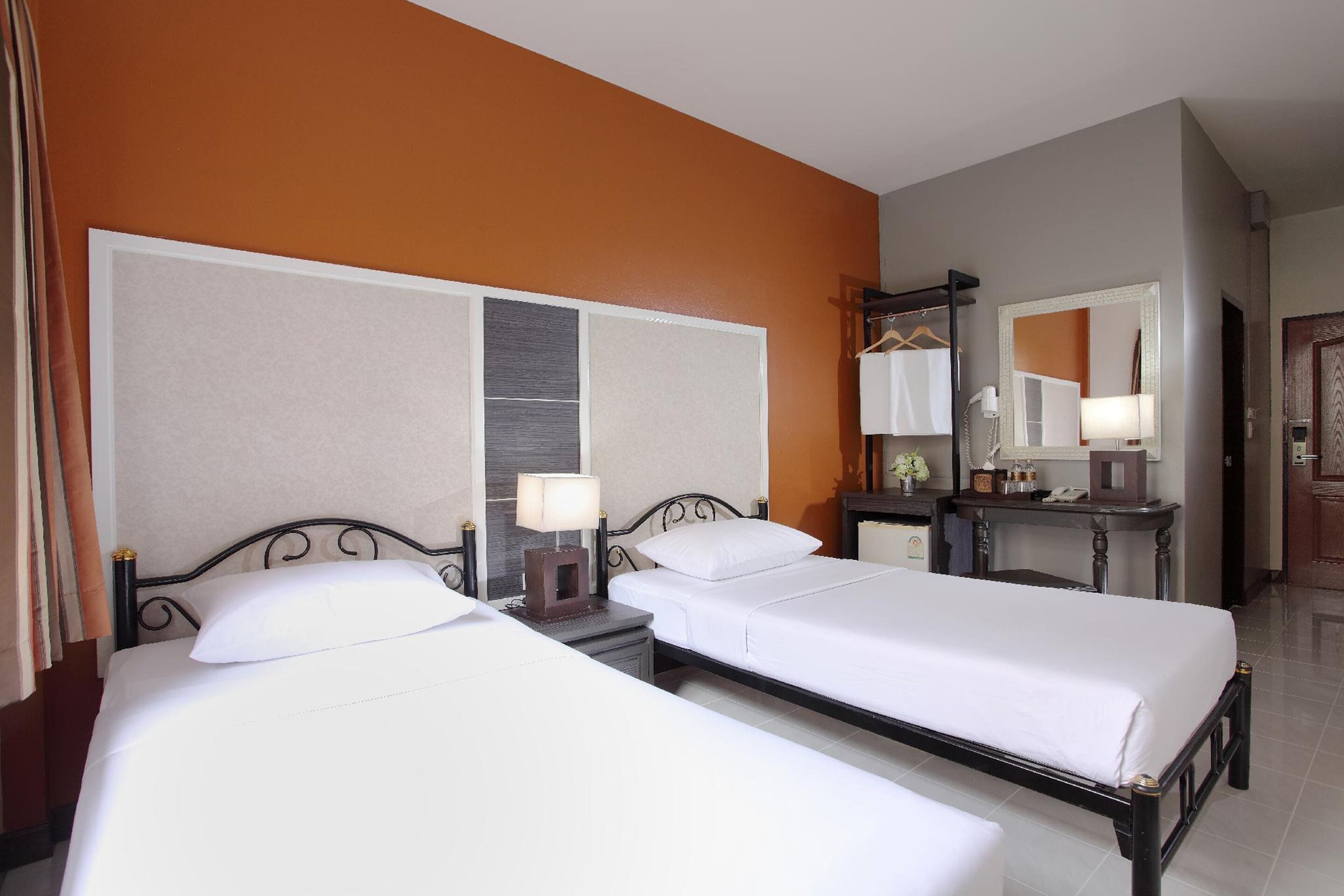 Une chambre d’hôtel avec deux lits, une table de chevet avec une lampe, une commode et un miroir.