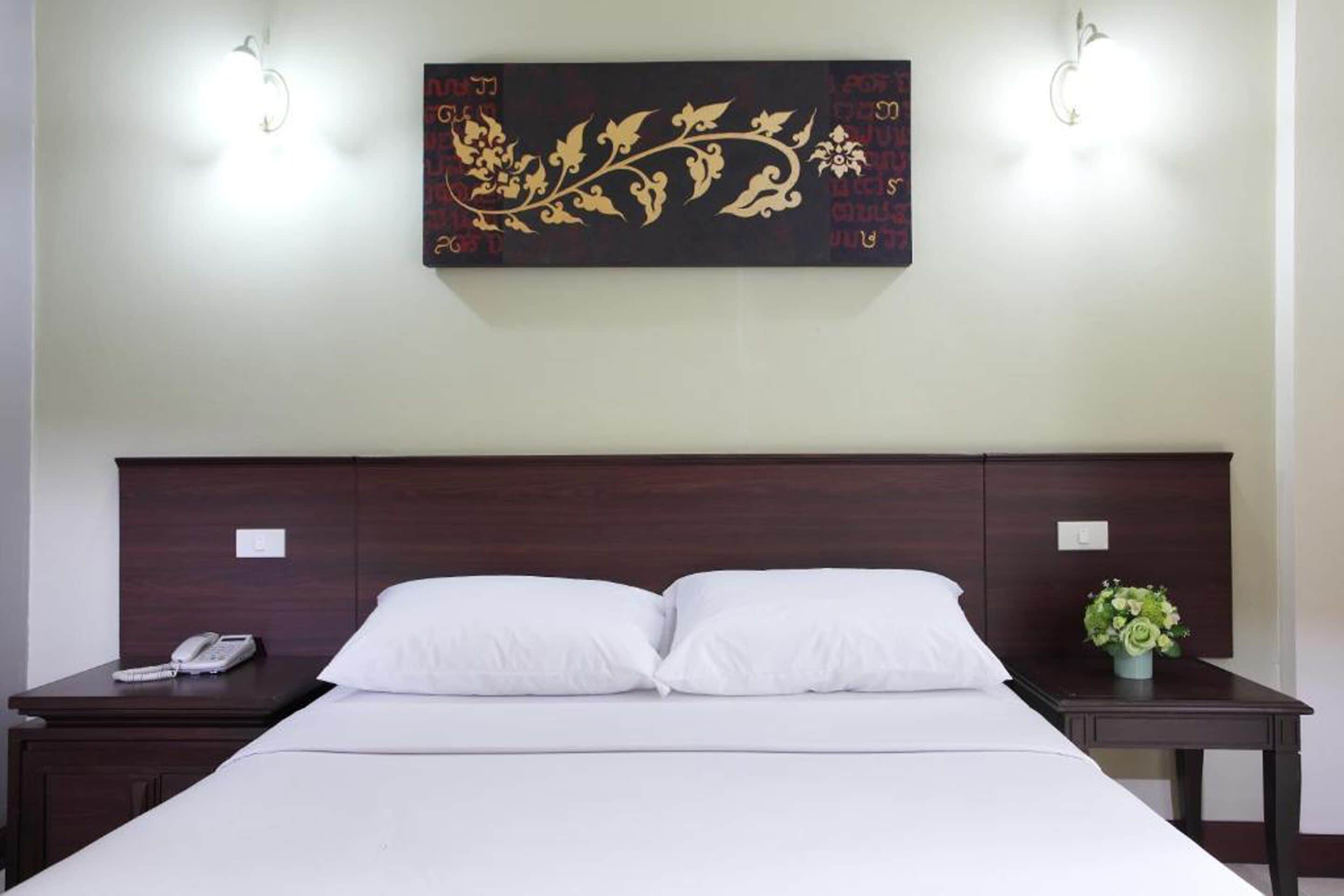 Habitación de hotel con una cama grande, dos mesitas de noche, una obra de arte en la pared y una mesita con un teléfono.