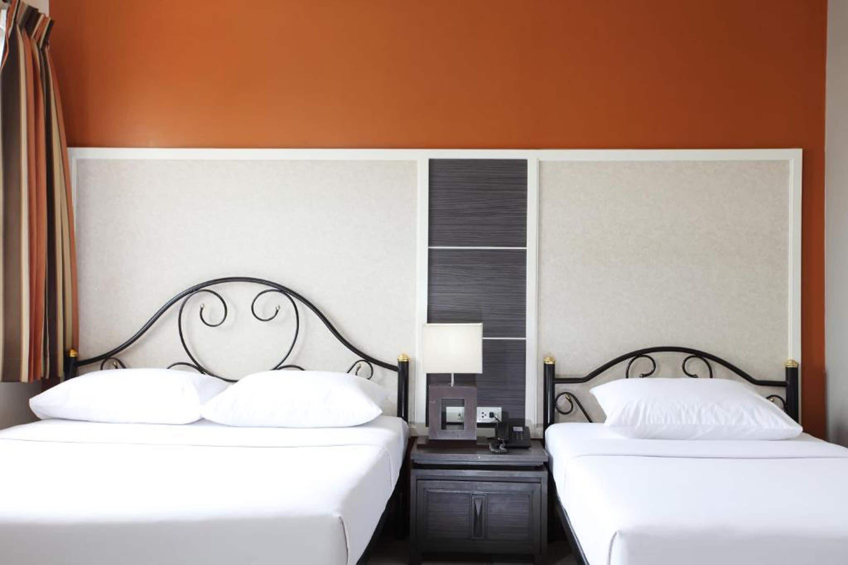 Una habitación de hotel con dos camas, una mesita de noche con lámpara y un panel en la pared.