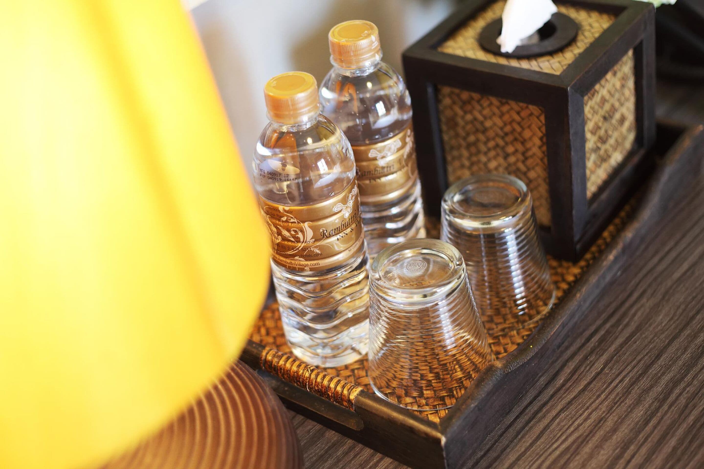 A tray with three water bottles and two glass tumblers on a woven mat.