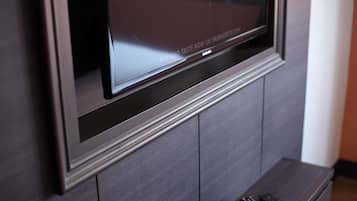 A flat-screen TV mounted on a dark wooden wall with a remote control on a small wooden stand below it.