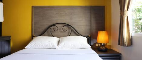 A bed with a wooden headboard, two white pillows, a nightstand with a lamp, and a window with curtains.