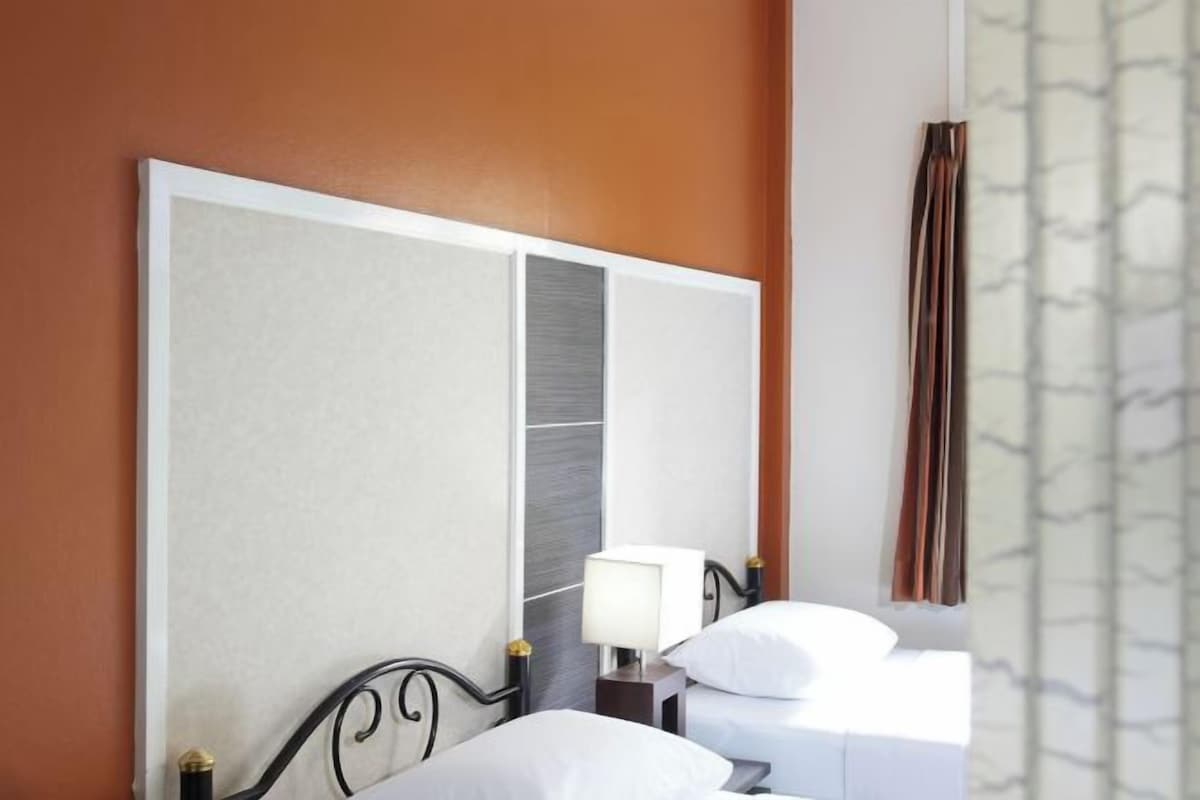 Quarto de hotel com uma cama grande, uma mesa de cabeceira com abajur e uma janela com cortinas.