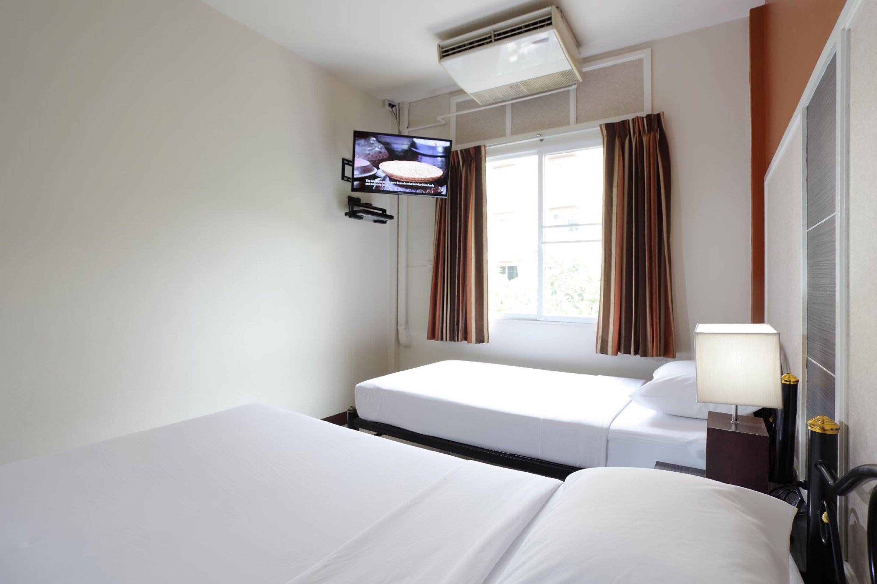A hotel room with two beds, a TV mounted on the wall, a window with curtains, and a bedside lamp.
