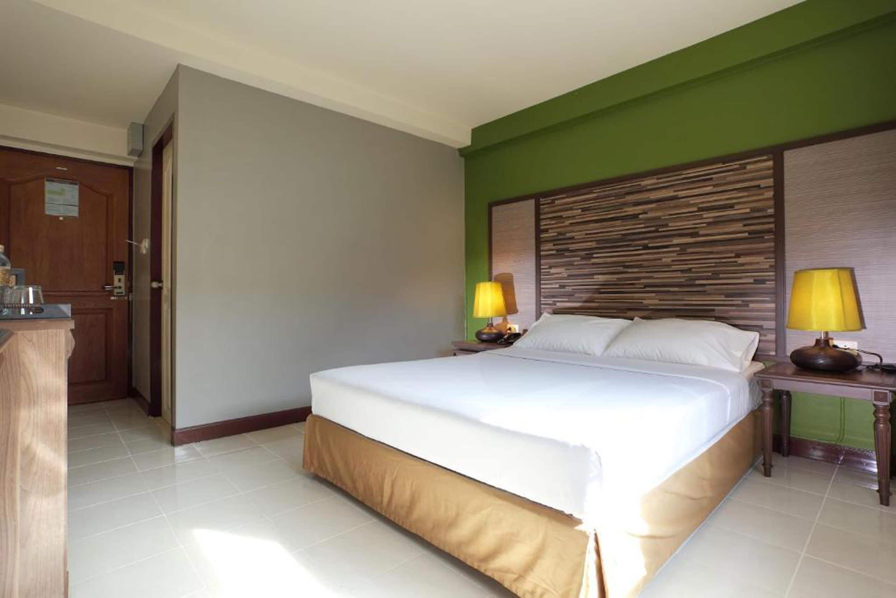 Una habitación de hotel con una cama grande, dos lámparas de noche, un cabecero de madera y una pared de acento verde.