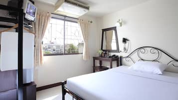 Une chambre d’hôtel avec un lit, un bureau équipé d’un ordinateur, une fenêtre avec des rideaux et un miroir fixé au mur.