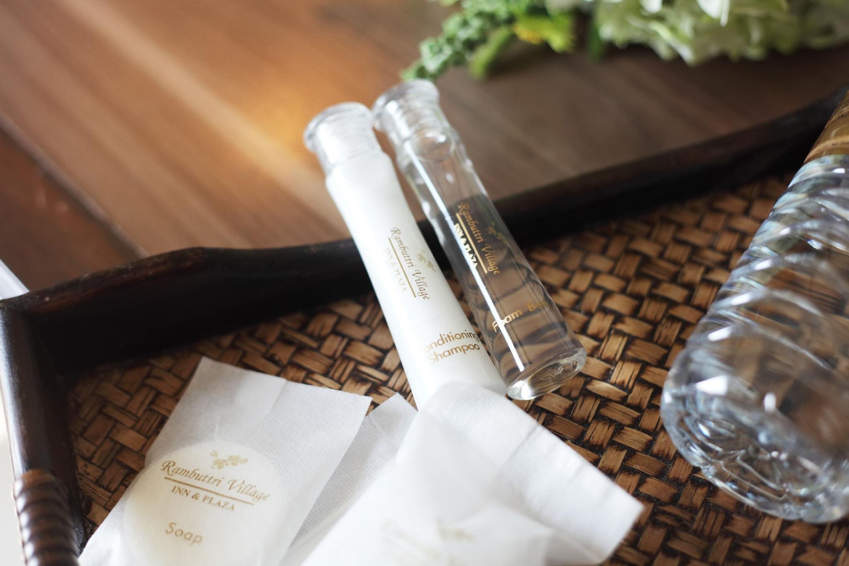 A tray with a bottle of shampoo, a bottle of conditioner, a bottle of soap, and a water bottle on a woven mat.