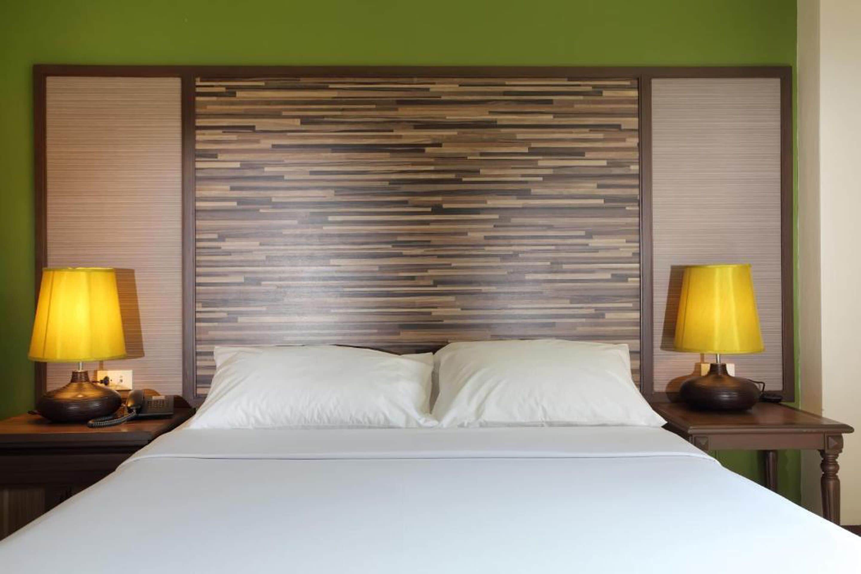 A hotel room with a bed, two bedside lamps, and a wooden headboard.