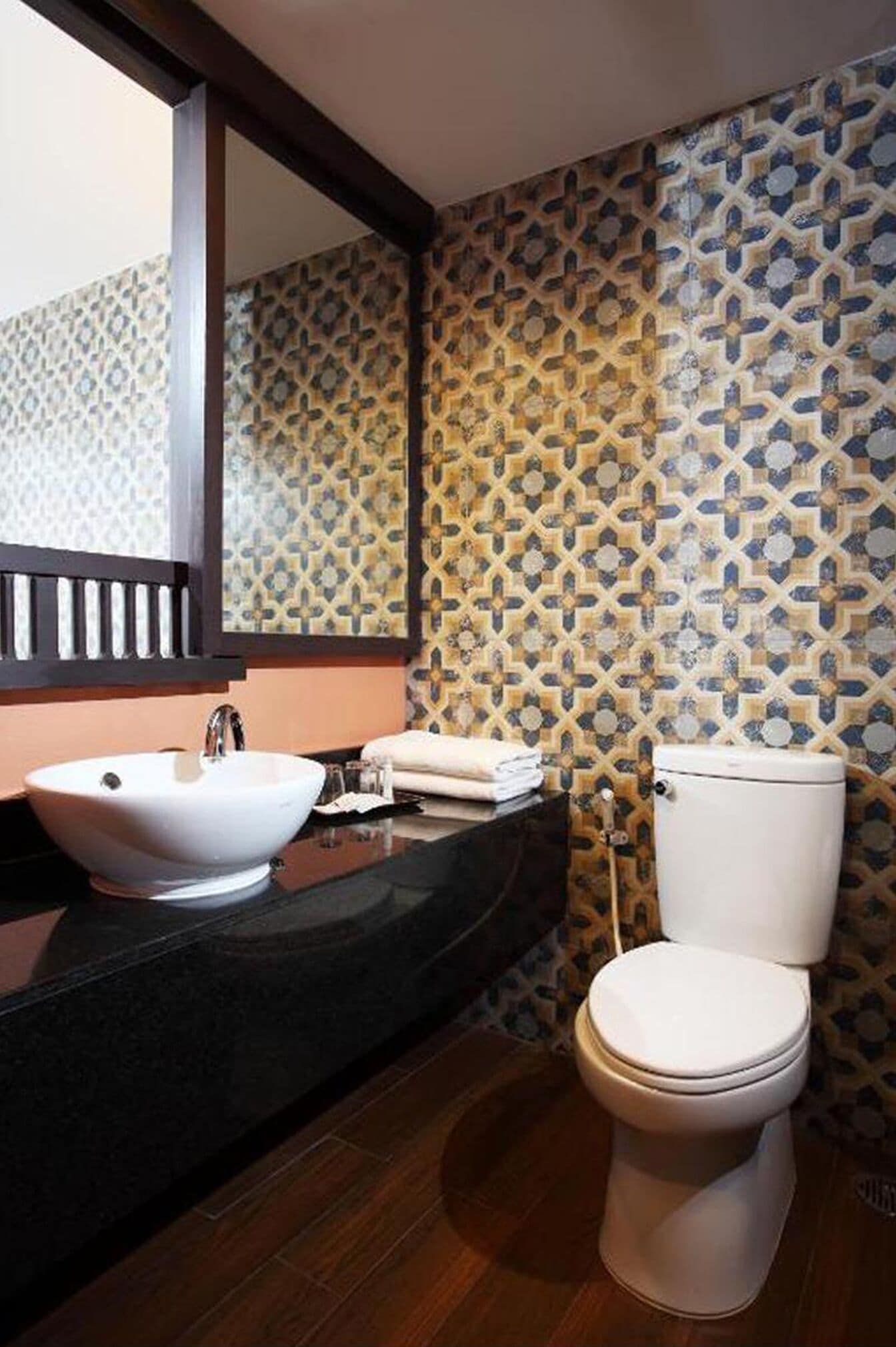 A bathroom with a white sink, a toilet, and a mirror above the sink. The walls have a patterned tile design.