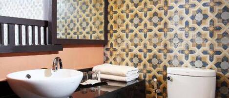 Un baño con un lavabo blanco, un inodoro y un espejo sobre el lavabo. Las paredes tienen un diseño de azulejos con motivos.