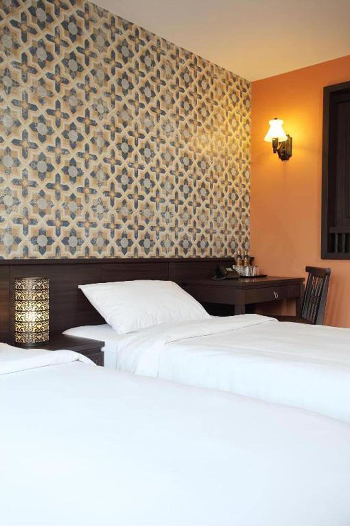 Hotelkamer met een patroonbehang, een nachtkastje met lamp en een bed met witte lakens.