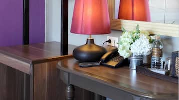 A bathroom with a wooden vanity, a mirror, a red lamp, a white towel, and a small vase with white flowers.