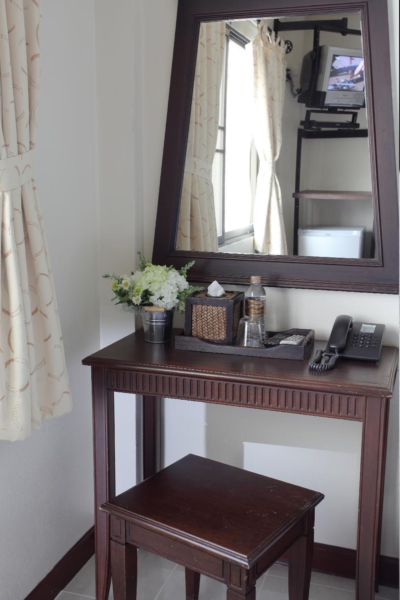 A wooden console table with a mirror above it, a small stool in front, and a vase with flowers.