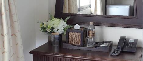 A wooden console table with a mirror above it, a small stool in front, and a vase with flowers.