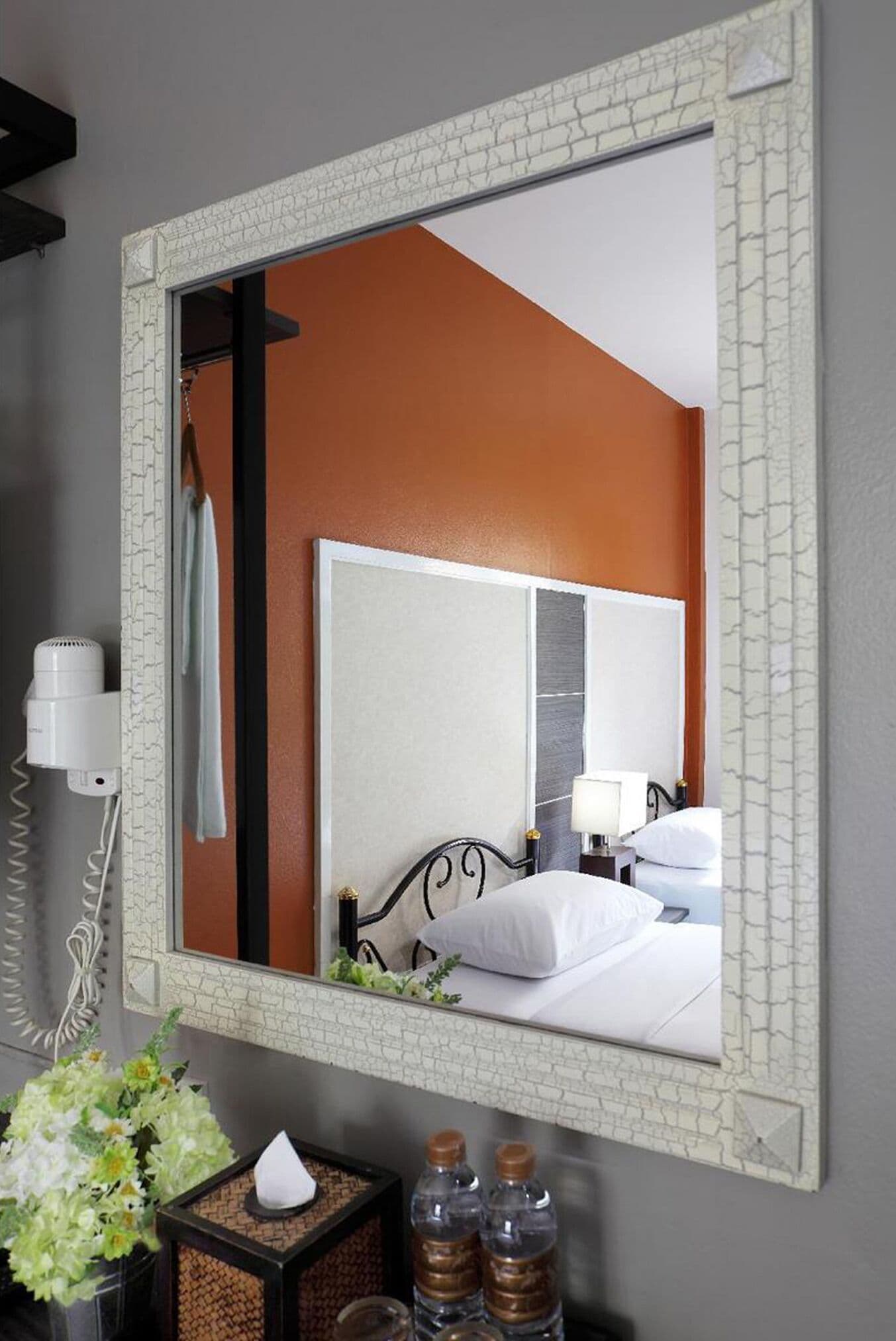 A hotel room with a large mirror, a bed with white linens, a bedside table with a lamp, and a hairdryer on the wall.