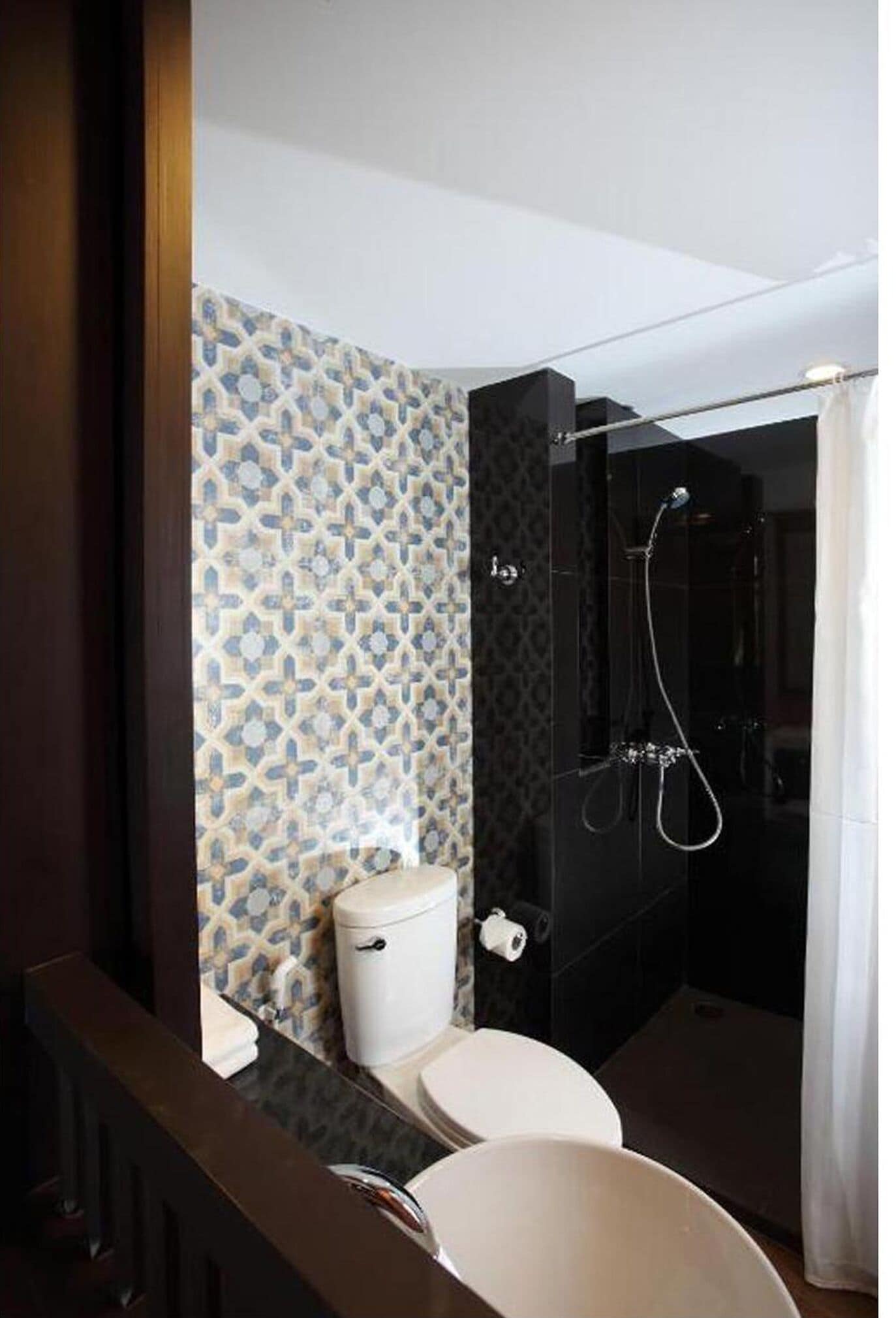 Un baño moderno con pared de azulejos estampados, inodoro, lavamanos y zona de ducha.