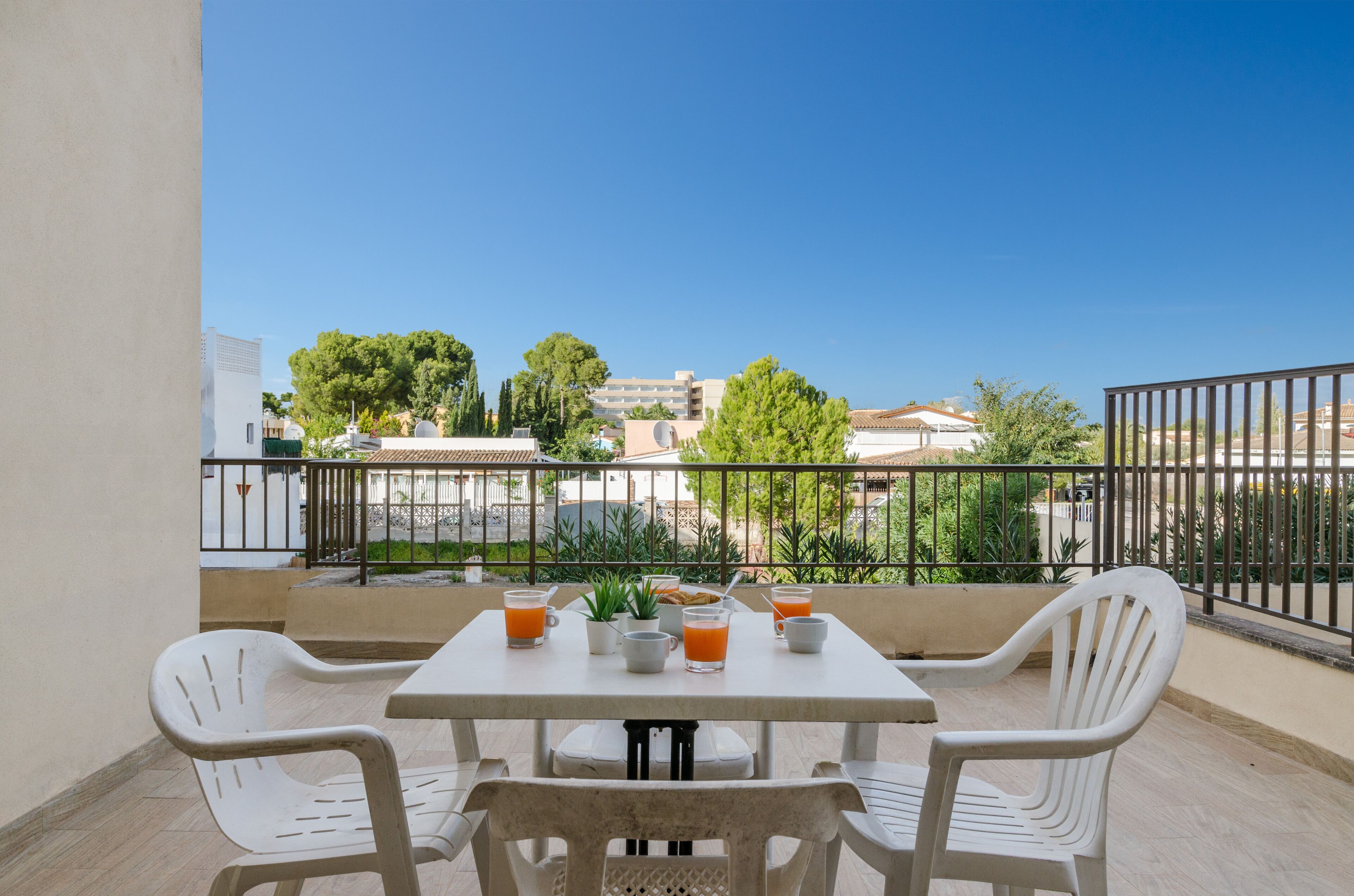 A balcony with a table set for two, featuring a breakfast arrangement including orange juice and a small plant.