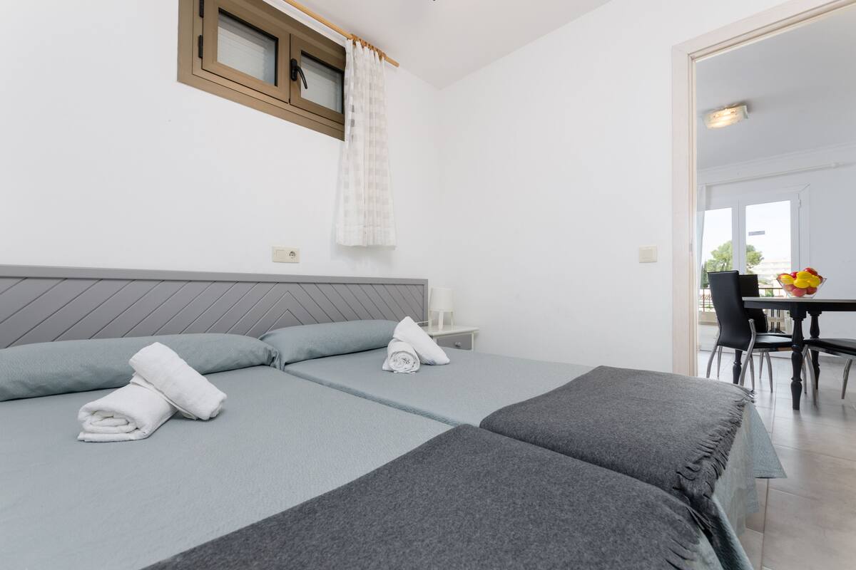 A hotel room with two beds, a small table with chairs, and a view of the outside.