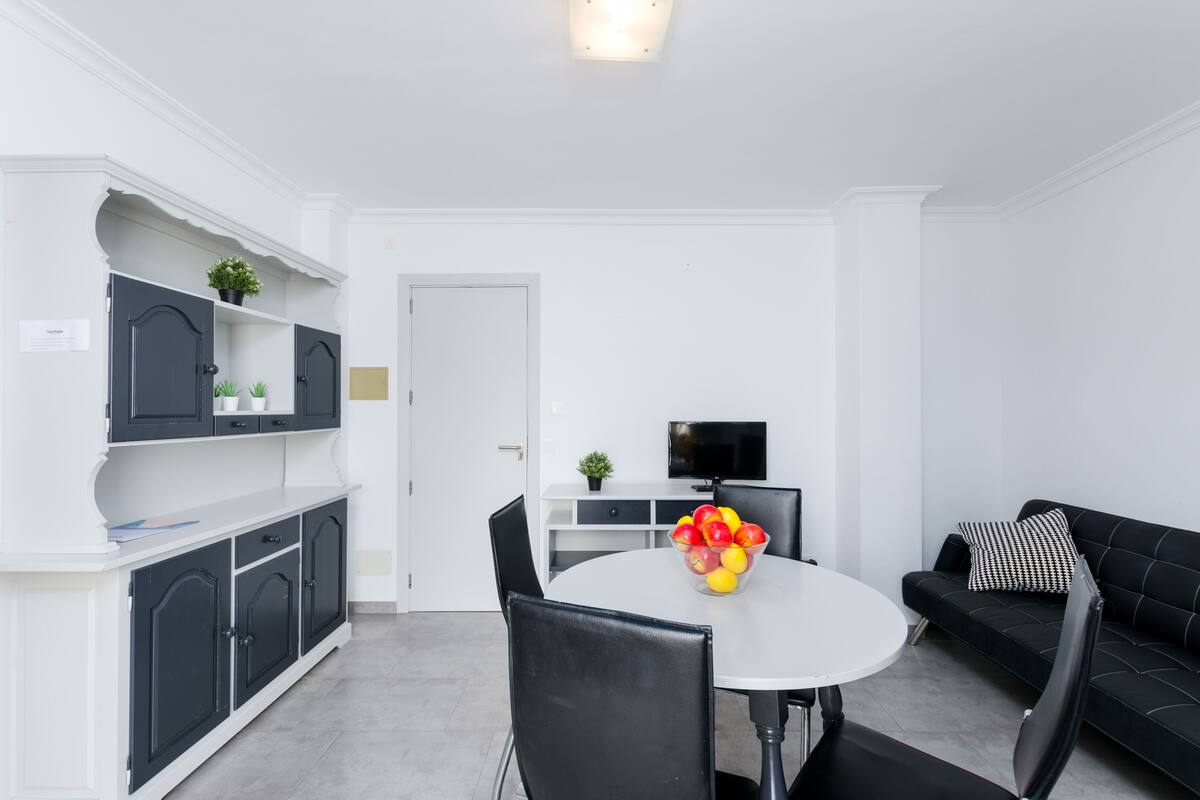 A modern living room with a round dining table, black leather sofa, and a TV.