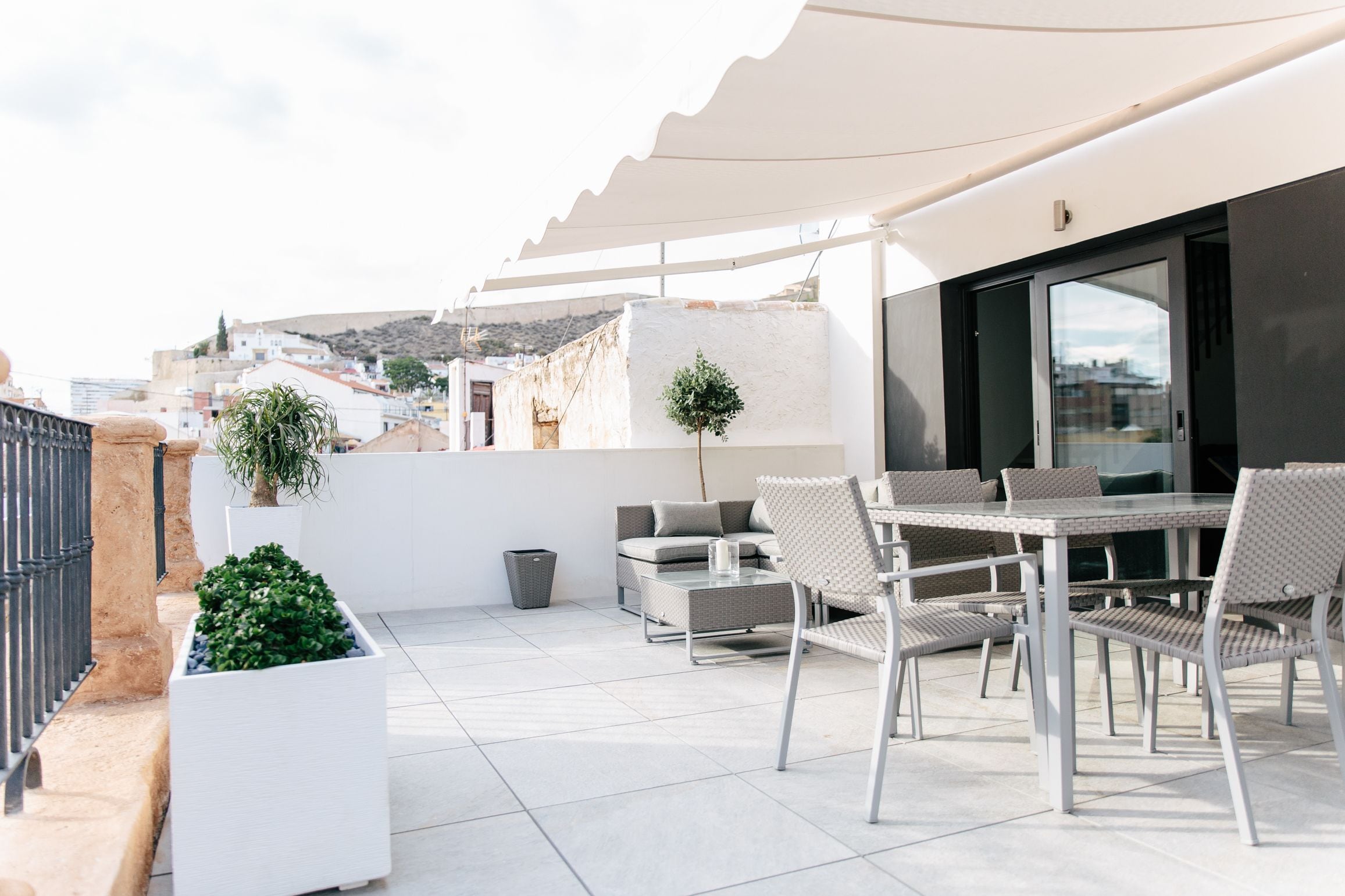 Terraço no telhado com mobiliário de exterior, uma planta em vaso e vista para a paisagem urbana.