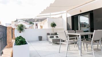 Terraço no telhado com mobiliário de exterior, uma planta em vaso e vista para a paisagem urbana.