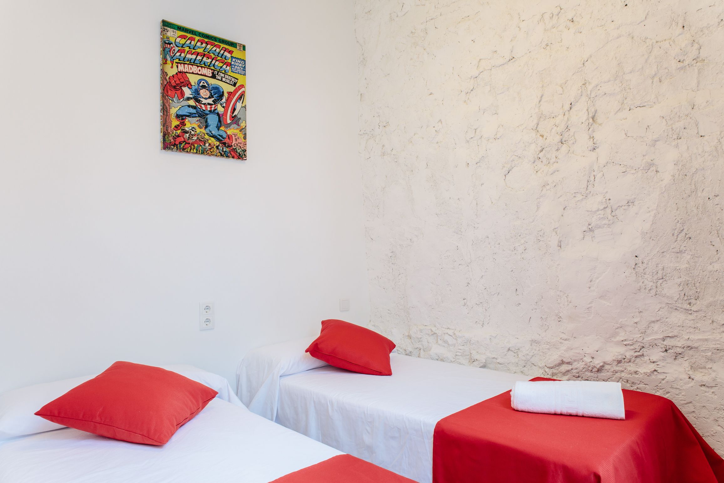 Una habitación con dos camas, cada una con una almohada roja y una manta blanca. Hay un cartel en la pared sobre las camas.