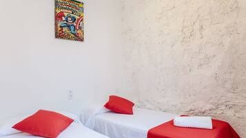 Una habitación con dos camas, cada una con una almohada roja y una manta blanca. Hay un cartel en la pared sobre las camas.