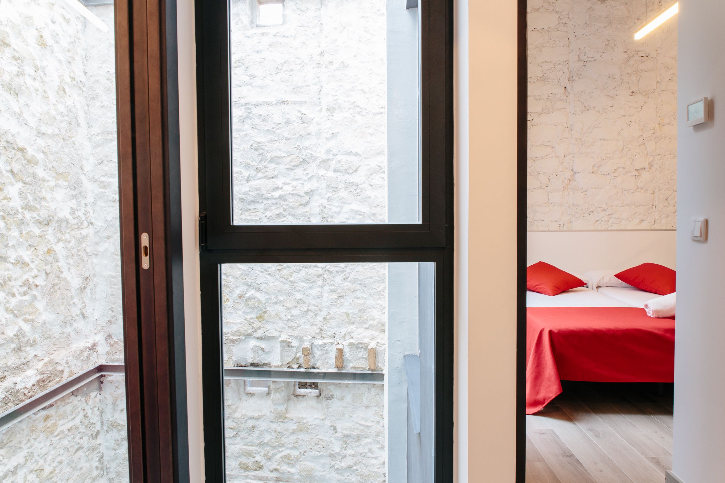 A room with a bed, a window, and a view of a stone wall.