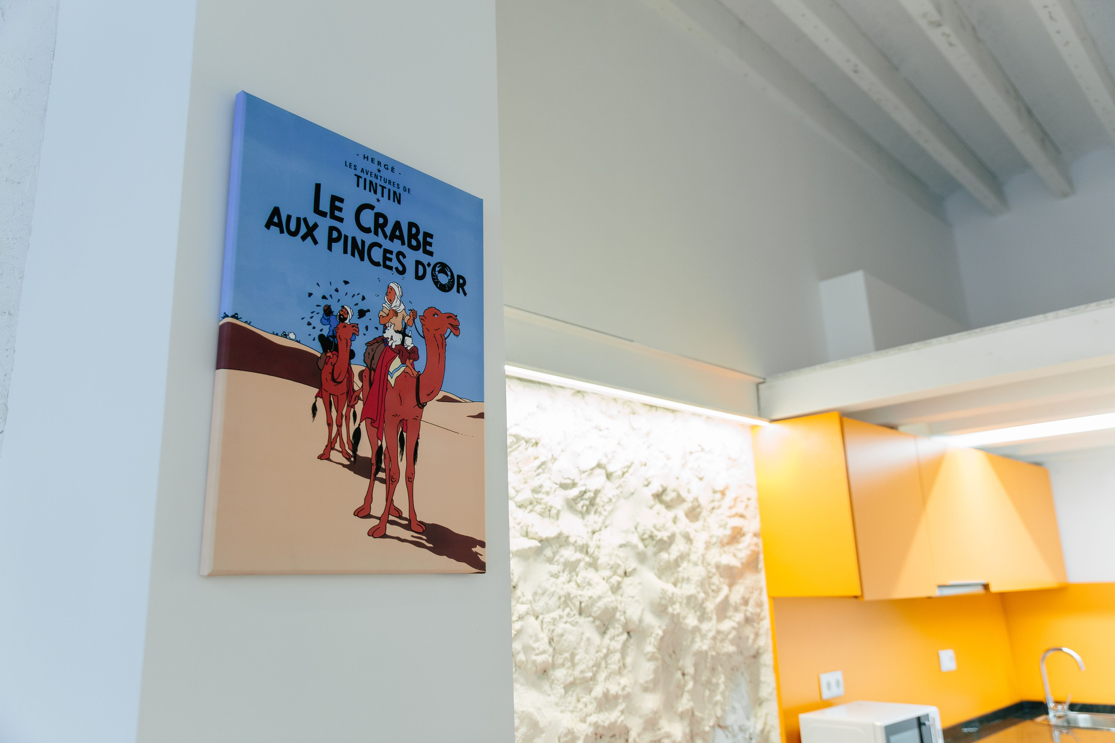 A poster of 'Le Crabe aux Pinces d'Or' in a room with a white textured wall and a bright yellow cabinet.