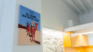 A poster of 'Le Crabe aux Pinces d'Or' in a room with a white textured wall and a bright yellow cabinet.