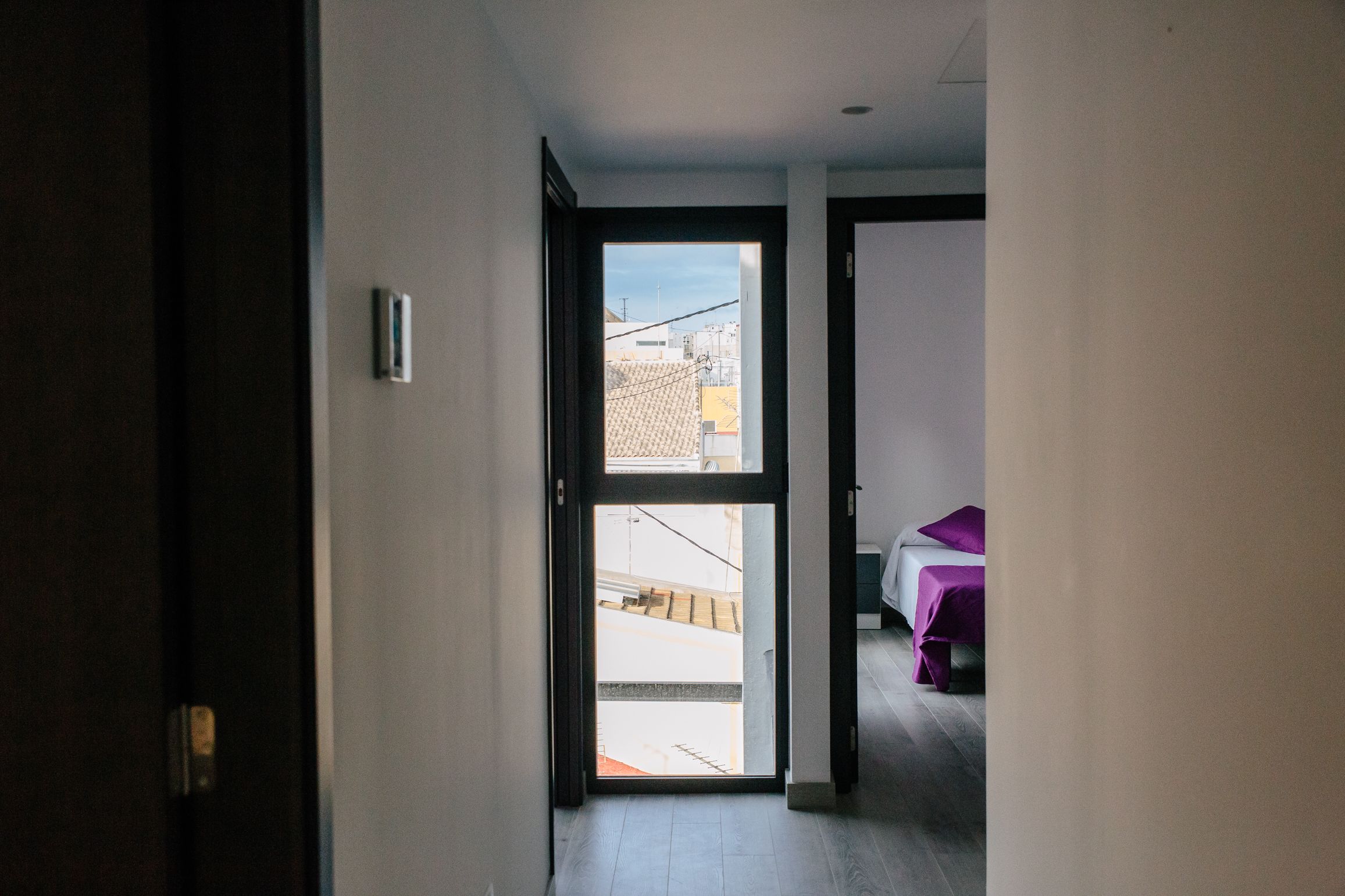 Un estrecho pasillo que da a un dormitorio con cama y ventana.