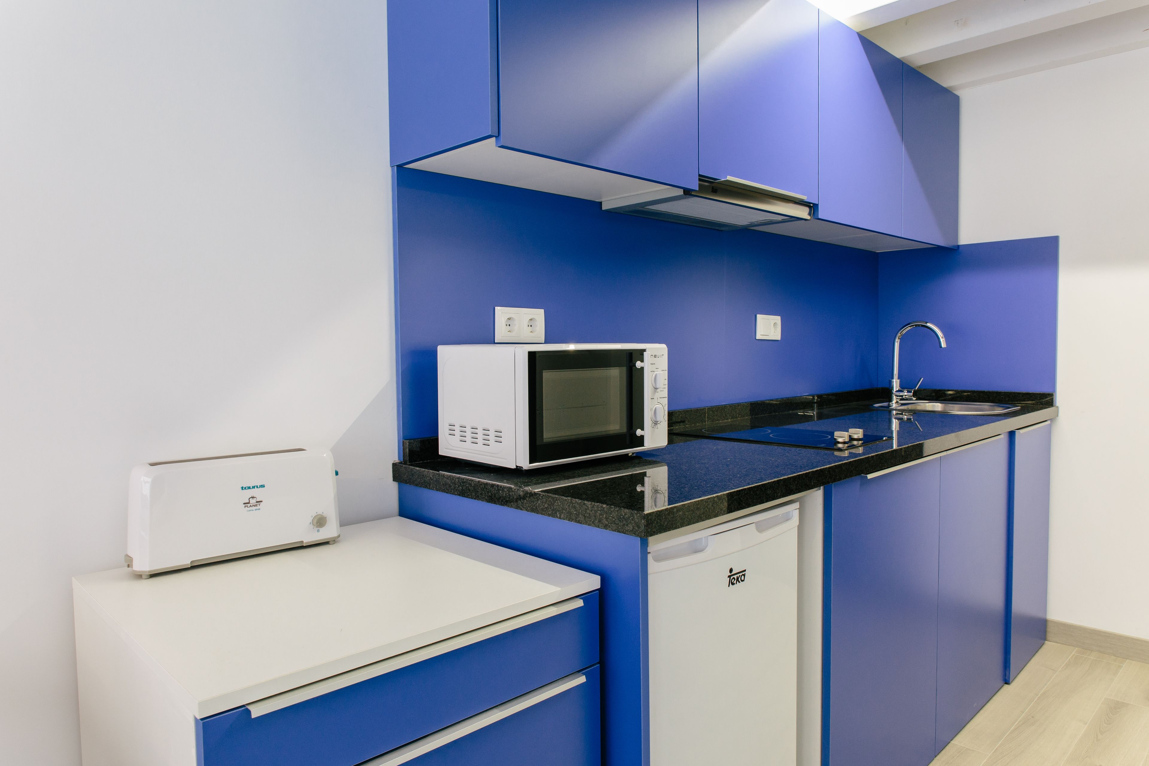 Une cuisine moderne avec des meubles bleus, un plan de travail blanc, un four à micro-ondes, un grille-pain et un lave-vaisselle.