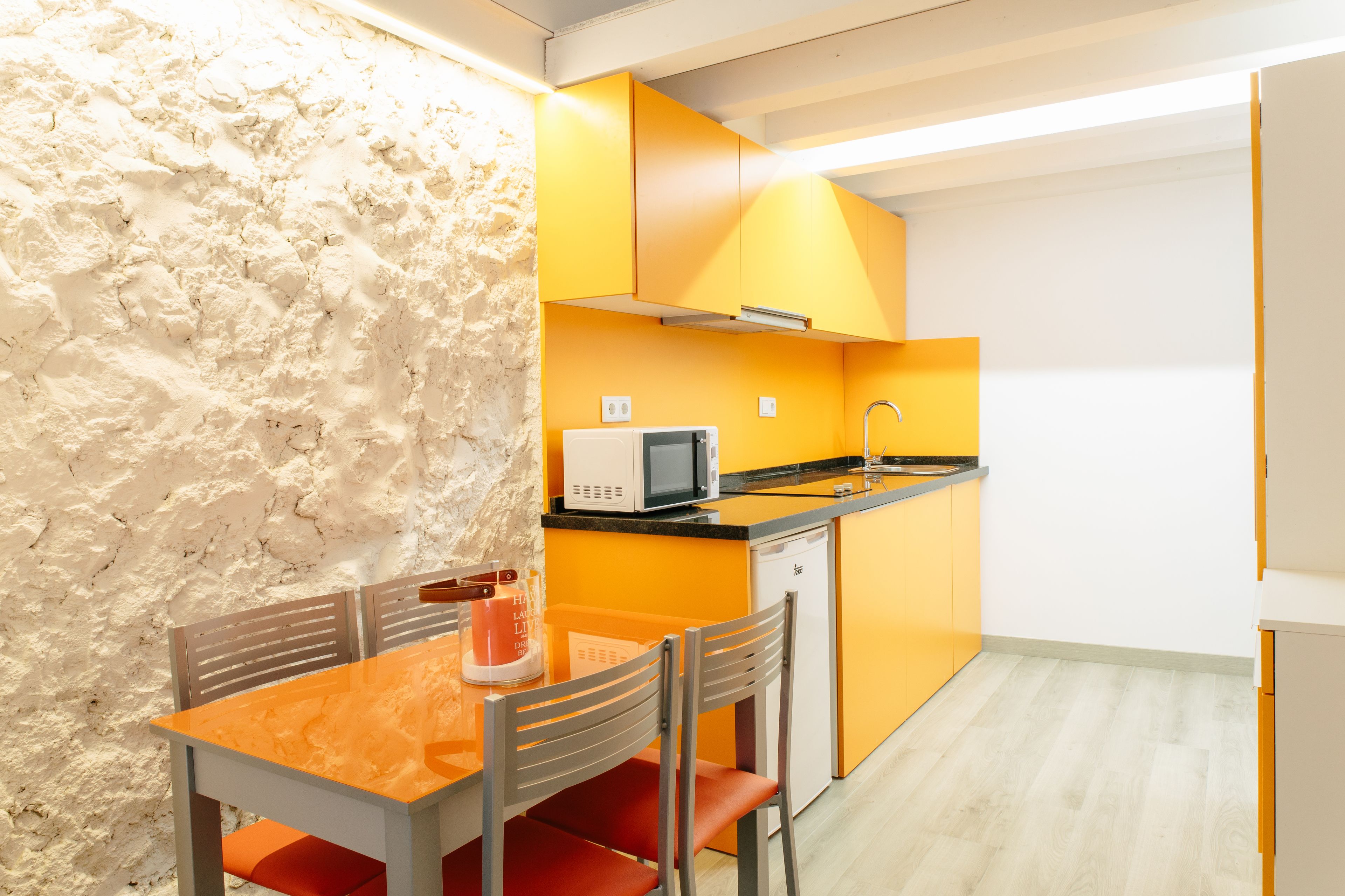 Een kleine keuken met een eethoek, met een magnetron, spoelbak en oranje kastjes.