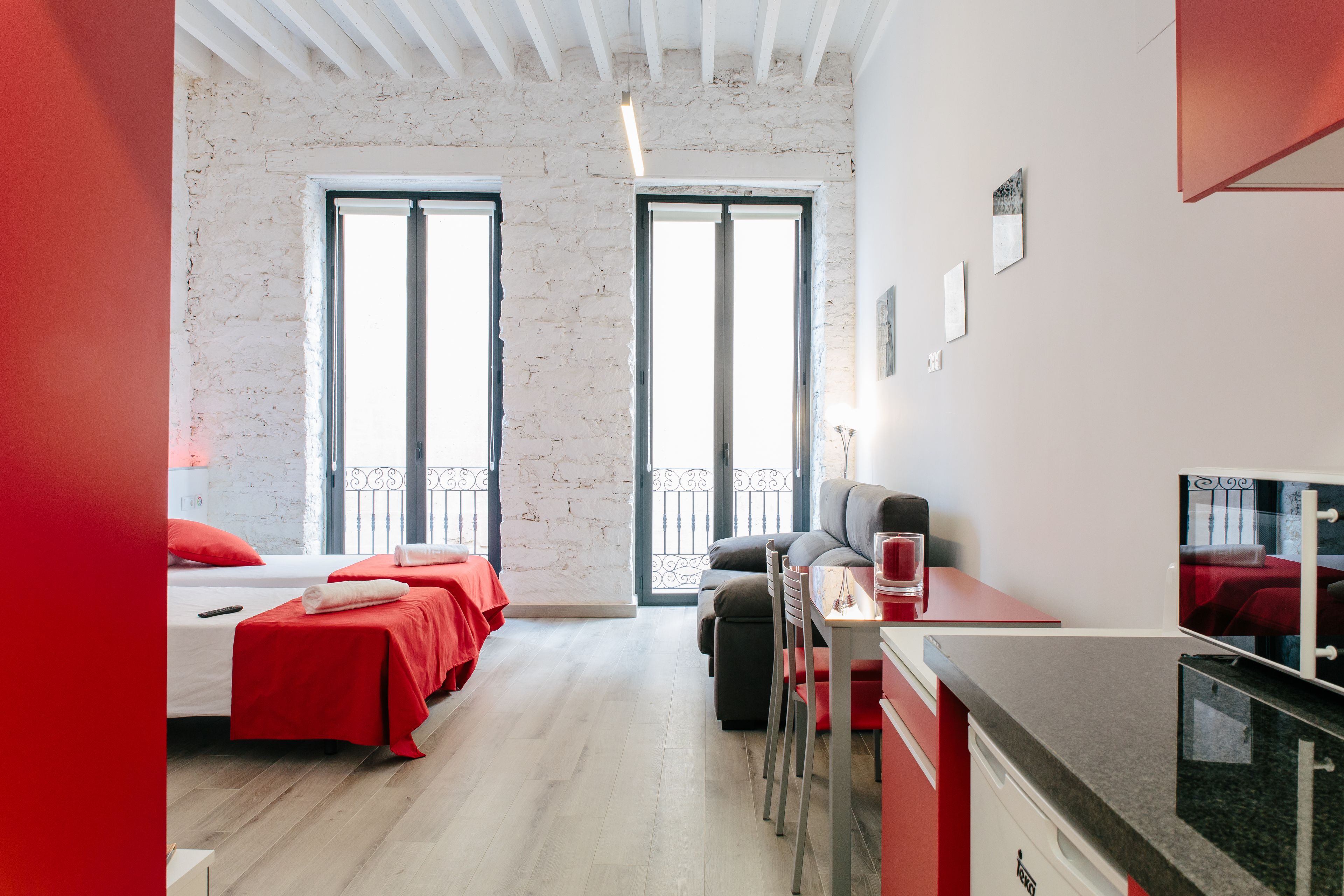 A modern hotel room with two beds, a dining area, and large windows.