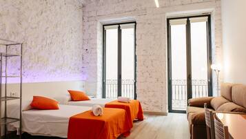 A hotel room with two beds, a sofa, a table, and a balcony.